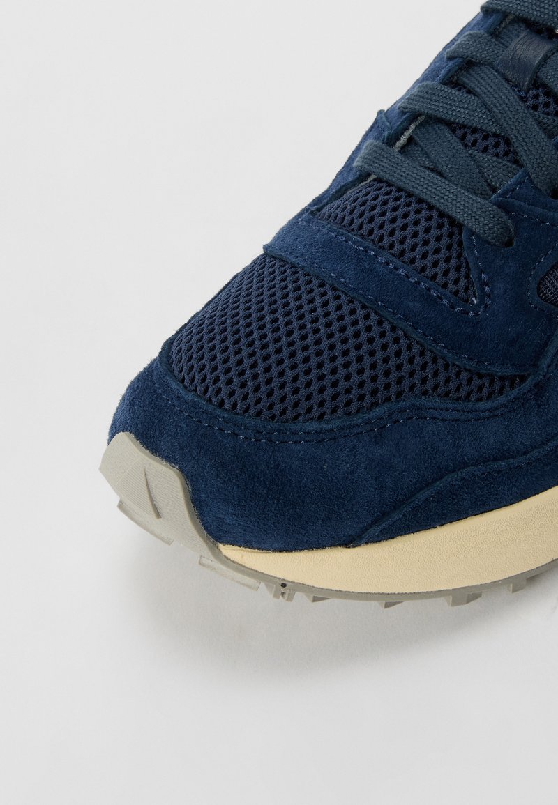 Sneaker blu navy che presenta una combinazione di materiali in rete e camoscio, con una tomaia testurizzata e una suola chiara.