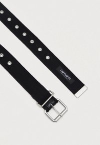 Ceinture en tissu tissé noir avec boucle en argent, œillets en métal, embout en métal et étiquette logo Carhartt sur fond blanc uni.