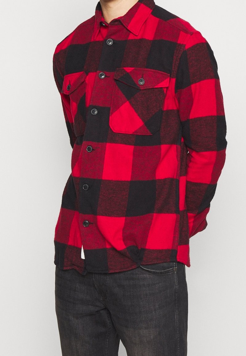 Camicia in flanella a scacchi rossi e neri con pattina frontale, due tasche sul petto e colletto classico. Realizzata in tessuto morbido e testurizzato.