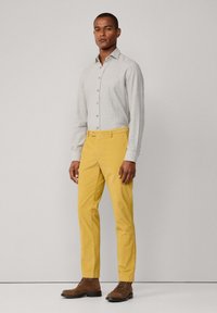 Vaaleanharmaa napapaita yhdistettynä kapeisiin keltaisiin housuihin. Ruskeat mokkasiinit korostavat ilmettä. Sujuva pinta modernilla leikkauksella.