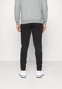 Pantaloni jogger neri a gamba affusolata con polsini elastici, abbinati a scarpe da ginnastica bianche. Il modello indossa un maglione grigio a maniche lunghe.