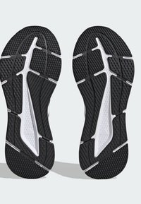 Musta urheilujalkineen pohja, jossa on teksturoitu kumipinta, ja jossa on yksityiskohtainen urakuvio sekä valkoisia yksityiskohtia, suunniteltu pitämään ja kestämään.