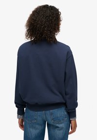 Sudadera azul marino con cuello alto, puños y dobladillo acanalados. Presenta detalles a rayas en los puños y un tejido suave y texturizado.