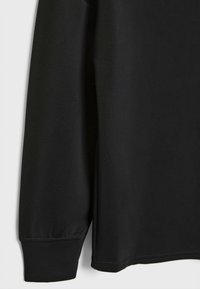 Manche de chemise noire à manches longues avec poignet élastique et texture de tissu lisse suspendue sur un fond blanc.