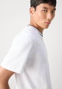Camiseta blanca de manga corta con cuello redondo y borde negro, fabricada en un tejido suave y con un diseño sencillo y elegante.