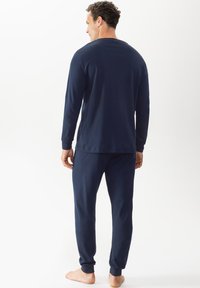 Ensemble de pyjama à manches longues bleu marine en tissu doux, comprenant un col ras du cou, une coupe décontractée et des poignets élastiques sur le pantalon. Coutures plates visibles.