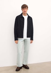 Musta samettitakki napilla edessä, valkoinen pyöreäkauluksinen t-paita, vaaleansiniset suorat farkut ja tummanruskeat platform-kengät.