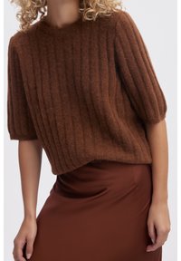 Pull en Maille côtelée marron avec des manches bouffantes courtes, fabriqué en matériau pelucheux ; associé à une jupe en satin marron lisse.
