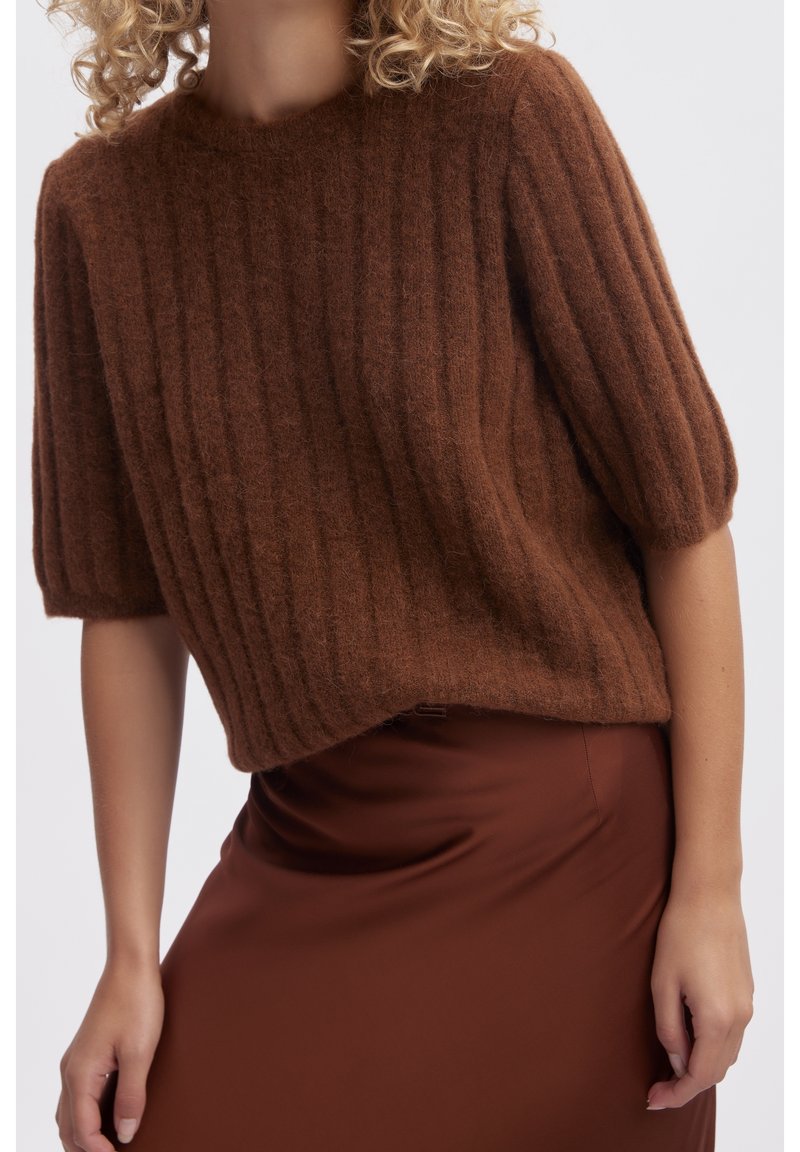 Pull en Maille côtelée marron avec des manches bouffantes courtes, fabriqué en matériau pelucheux ; associé à une jupe en satin marron lisse.