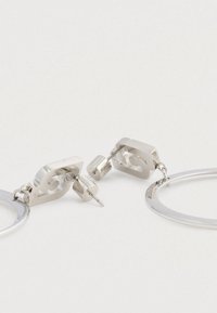 Orecchini a cerchio in argento con una forma circolare e un accento con logo. Realizzati in metallo con una finitura lucida e chiusura posteriore.