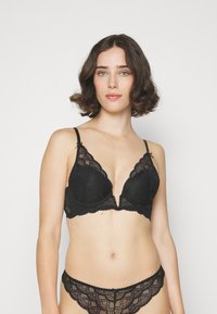 Melnas mežģīņu bralette ar dziļu V formas dekoltē un regulējamiem siksnām, ar viļņainām malām. Atbilstoši mežģīņu apakšbikses ar viļņainu dizainu.