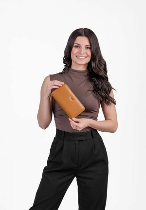 Hnědá kožená peněženka, obdélníkový tvar, hladký povrch. Model drží peněženku, má na sobě těsně přiléhající top a kalhoty s vysokým pasem. Bílý pozadí.