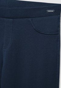 Granatowe spodnie elastyczne o gładkiej teksturze, z jedną przednią kieszenią i szerokim elastycznym pasem. Mały akcent logo na pasie.