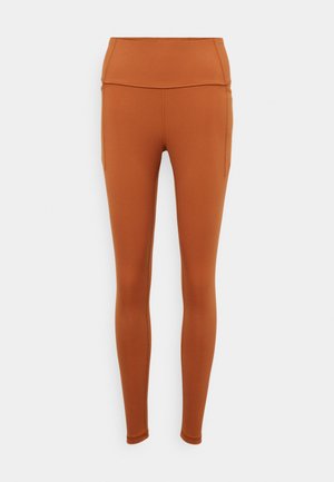 Bronz színű sportleggings magas derékkal, sima textúrával és oldalsó zsebekkel, tapered lábakkal és minimalista dizájnnal.