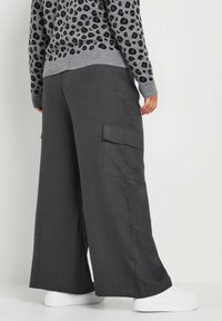 Grijze cargo-broek met wijde pijpen, gemaakt van textuurstof, met zijzakken en een relaxte pasvorm, gecombineerd met een grijze trui met luipaardprint.
