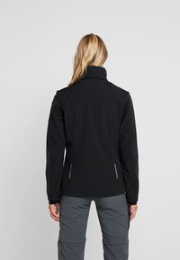 Zwarte softshell jas met een hoge kraag, voorzien van witte accenten en een aansluitend ontwerp. Glad oppervlak, rekbare stof en geen zichtbaar beslag.