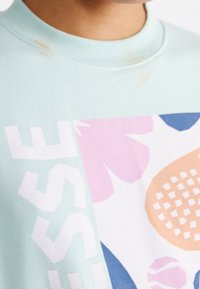 Felpa azzurra chiara con un grande design grafico caratterizzato da motivi floreali rosa, arancio e blu e lettering a blocchi. Texture morbida.