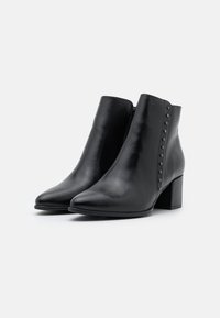 Botas de cuero negras hasta el tobillo con puntera afilada, tacón cuadrado y tachuelas decorativas a lo largo del costado. Textura suave y diseño minimalista.