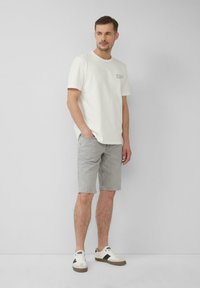 T-shirt en coton gris clair à manches courtes avec un texte imprimé sur le devant, associé à un short en jean gris et des baskets blanches avec des accents noirs.