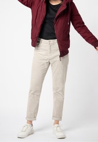 Beige kordflibbukser med avsmalnande ben, uppvikta fållar och knäppning fram, kombinerat med en vinröd jacka och vita sneakers.