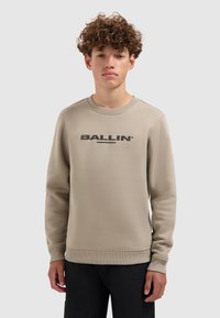 Lichtbeige sweatshirt gemaakt van zachte stof, met een ronde hals, geribde manchetten en een groot zwart "BALLIN" logo op de borst.