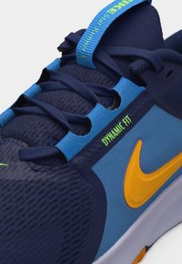 Κοντινό πλάνο μπλε και ναυτικού μποτάκι τρεξίματος με κίτρινο λογότυπο Nike, μπλε κορδόνια και το κείμενο «DYNAMIC FIT» στην πλευρική επιφάνεια.