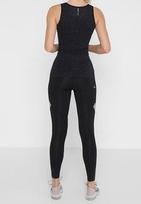 Czarny bezrękawnik sportowy z teksturowanym wzorem, w połączeniu z czarnymi legginsami z szarymi akcentami o dopasowanym kroju.