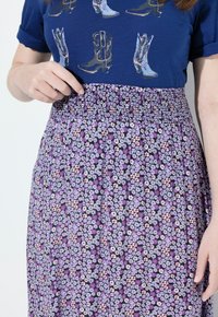Gonna maxi floreale viola con vita smock, caratterizzata da piccoli fiori multicolore su sfondo nero. Indossata con una t-shirt grafica blu.