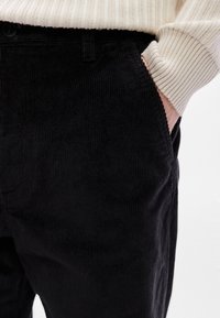 Μαύρο παντελόνι από κορδούρα με υφή στην επιφάνεια, με πλαϊνές τσέπες, εφαρμοστή μέση και λεία υφή υφάσματος. Συνδυασμένο με μπεζ πλεκτό πουλόβερ με ραβδώσεις.