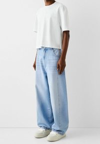 Vit kortärmad t-shirt och ljusblå vida jeans. Jeans har hög midja, framfickor och en ljustvättad denimstruktur. Kombinera med vita sneakers.