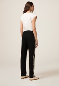 Zwarte broek met een rechte snit, voorzien van een witte zijkantstreep, elastische tailleband en gedragen met lichtgekleurde schoenen. Effen witte top.