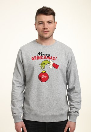 Grå sweatshirt med texten "God Jul, Grinch!", en illustration av Grinchen som håller en julprydnad, röda accenter.