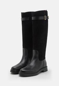 Schwarze knielange Stiefel aus Wildleder mit glatten Lederakzenten. Sie verfügen über eine texturierte Oberfläche, eine schlanke Silhouette und eine Schnallendetail.
