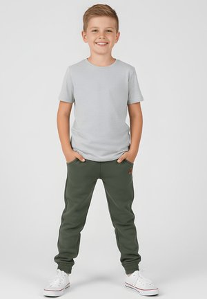 Szary t-shirt z krótkim rękawem i ciemnozielone dresowe spodnie zakończone ściągaczami. Białe trampki. Na spodniach znajduje się małe logo.