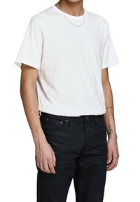 Witte katoenen t-shirt met een ronde hals, korte mouwen en een losse pasvorm, gecombineerd met zwarte denim jeans, met een tattoo op de arm.