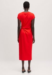Rotes, knielanges Kleid mit rundem Ausschnitt, kurzen Ärmeln und einer verdrehten Detail an der Rückseite. Hergestellt aus weichem, dehnbarem Stoff.