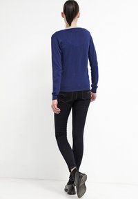 Tmavě modrý svetr s dlouhým rukávem a kulatým výstřihem, kombinovaný s přiléhavými černými džíny a černými kotníkovými botami. Hladká textura, minimalistický design.