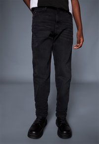 Jeans in denim nero con vestibilità slim, caratterizzati da un classico design a cinque tasche e una texture sottile, abbinati a stivali neri con stringhe.