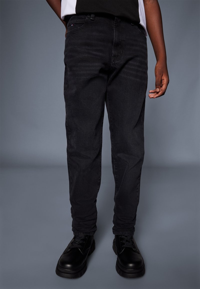 Jeans in denim nero con vestibilità slim, caratterizzati da un classico design a cinque tasche e una texture sottile, abbinati a stivali neri con stringhe.