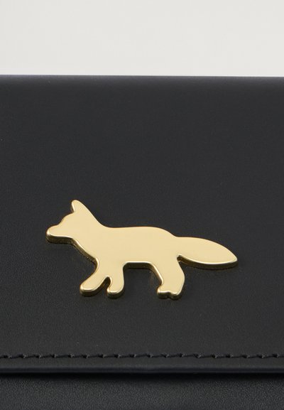 Μαύρο δερμάτινο πορτοφόλι με χρυσό μεταλλικό έμβλημα αλεπούς, με λεία υφή και καθαρές γραμμές, που αναδεικνύει τον παιχνιδιάρικο σχεδιασμό.