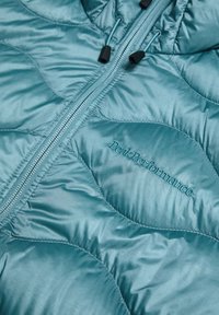 Quiltet teal puffer jakke med lynlås, hætte og "Peak Performance" logo i matchende broderi på forsiden.