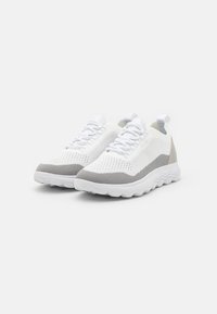 Zapatillas deportivas blancas y grises con un upper de punto texturizado, diseño de cordones y una suela blanca ondulada. Incluye un lazo en el talón.