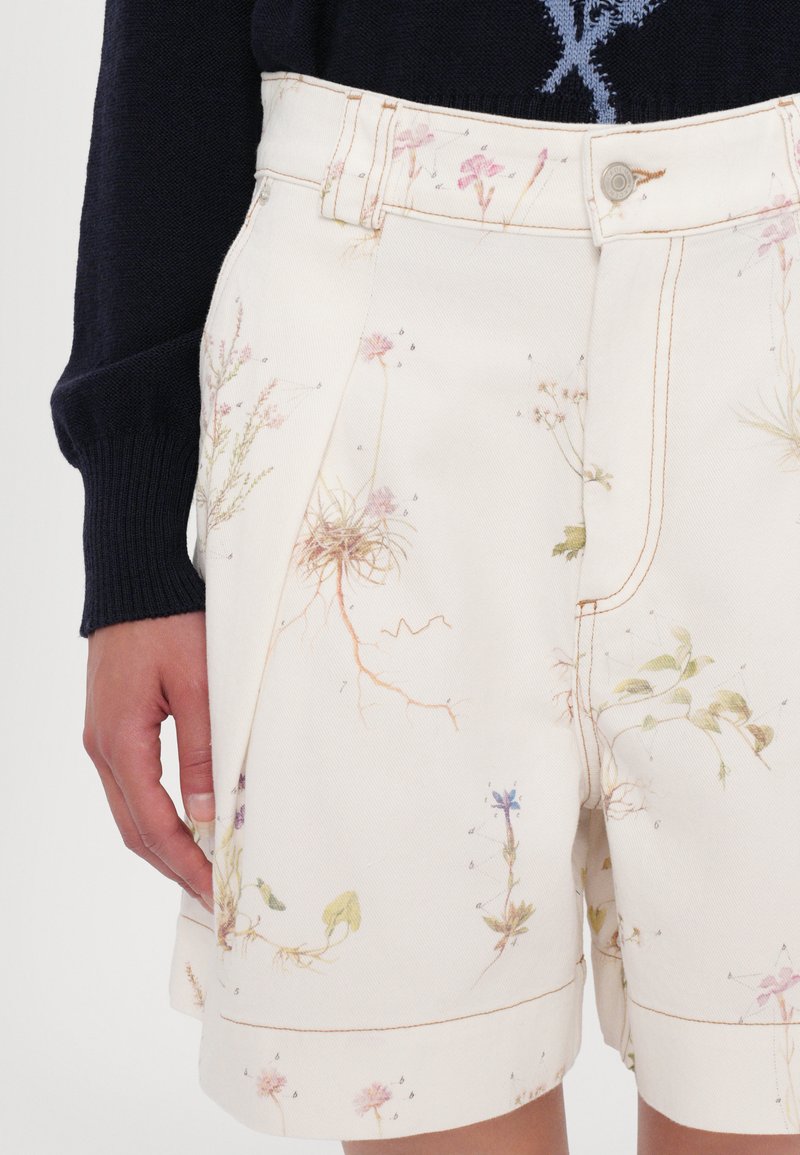 Shorts en toile imprimés floraux en crème, avec des illustrations de plantes, des coutures contrastées et un design classique à cinq poches avec fermeture par bouton.
