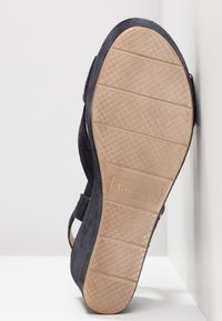 Semelle d'une sandale compensée noire avec une semelle extérieure en caoutchouc beige texturé et le nom de la marque "Tamaris" embossé au centre.