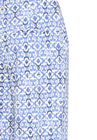 Primer plano de tela azul y blanca con motivos florales geométricos y una costura de bolsillo horizontal cosida.