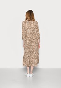 Abito midi marrone a fantasia con maniche a sbuffo e vita arricciata, indossato con sneakers bianche. Tessuto morbido con una silhouette fluida.