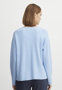 Svetlo modra rebrasta jopica z sproščenim krojem in spušenimi rameni, ki ima širok izrez in ravno spodnje rob. Struktura pletenega materiala.