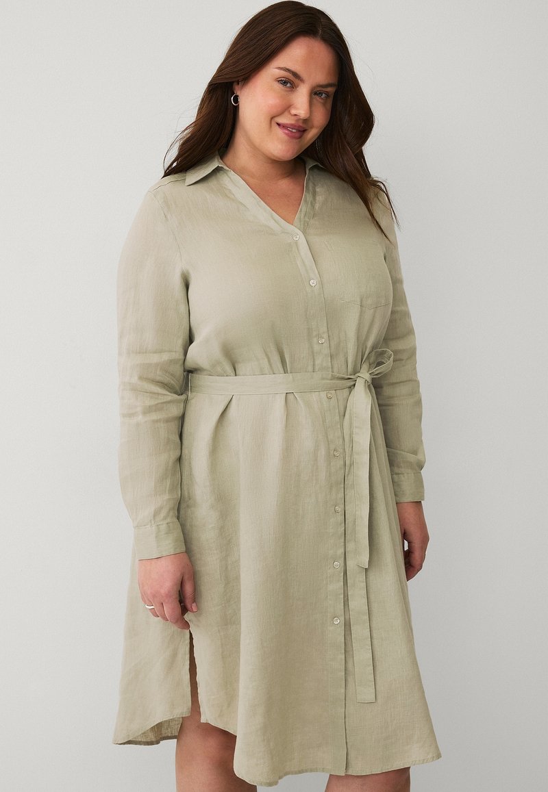 Abito camicia verde chiaro a maniche lunghe con bottoni frontali, vita con cintura e spacchi laterali. Realizzato in un tessuto leggero e testurizzato.