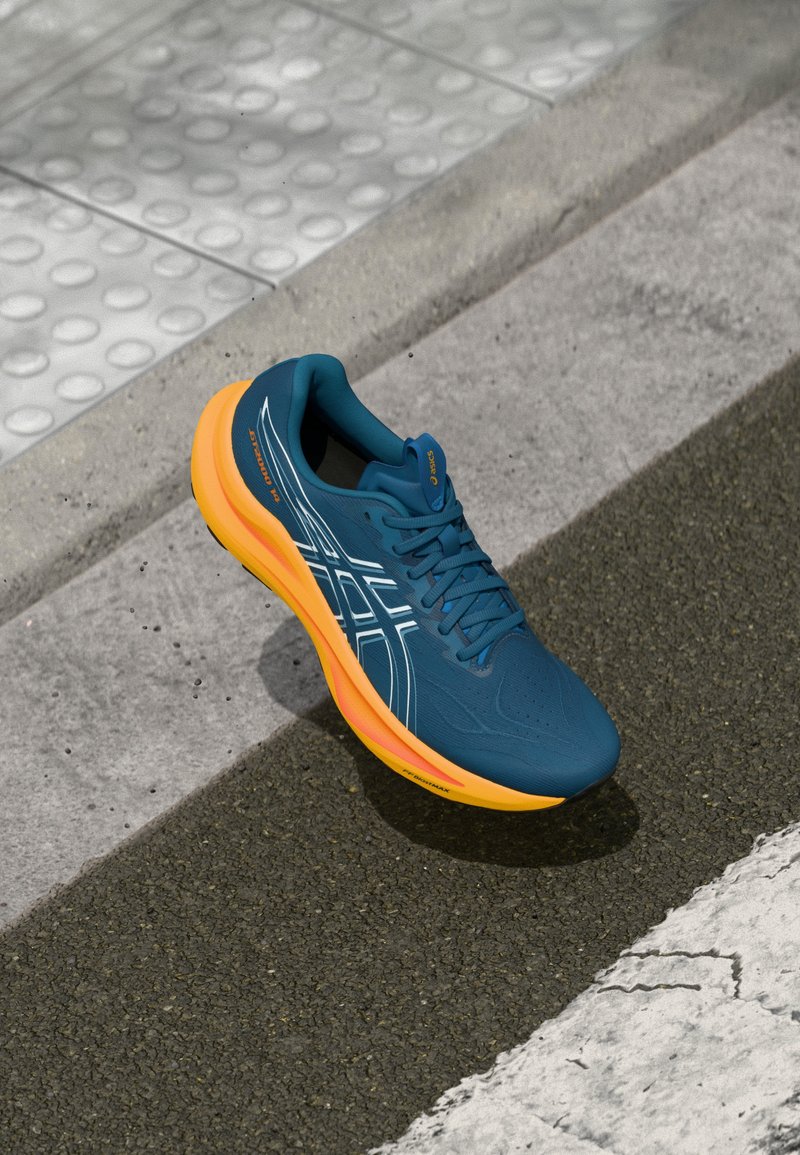 Hardloopschoen met een bovenwerk van blauw mesh, een oranje tussenzool en witte accenten. Kenmerken zijn een gestructureerde zool en platte veters voor een stevige pasvorm.