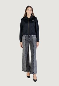 Felpa nera con zip e colletto, due tasche frontali, abbinata a jeans grigi a gamba larga con un contrasto di colore scuro e chiaro.